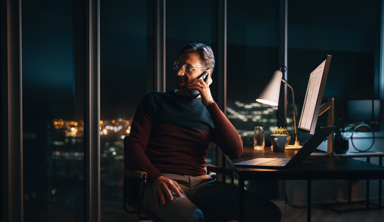 Man on a phone call beside a city window at night
