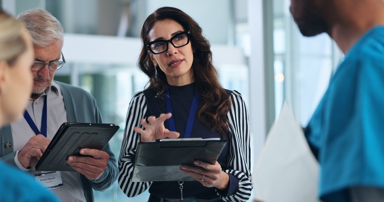 Healthcare administrator briefing colleagues while holding a tablet