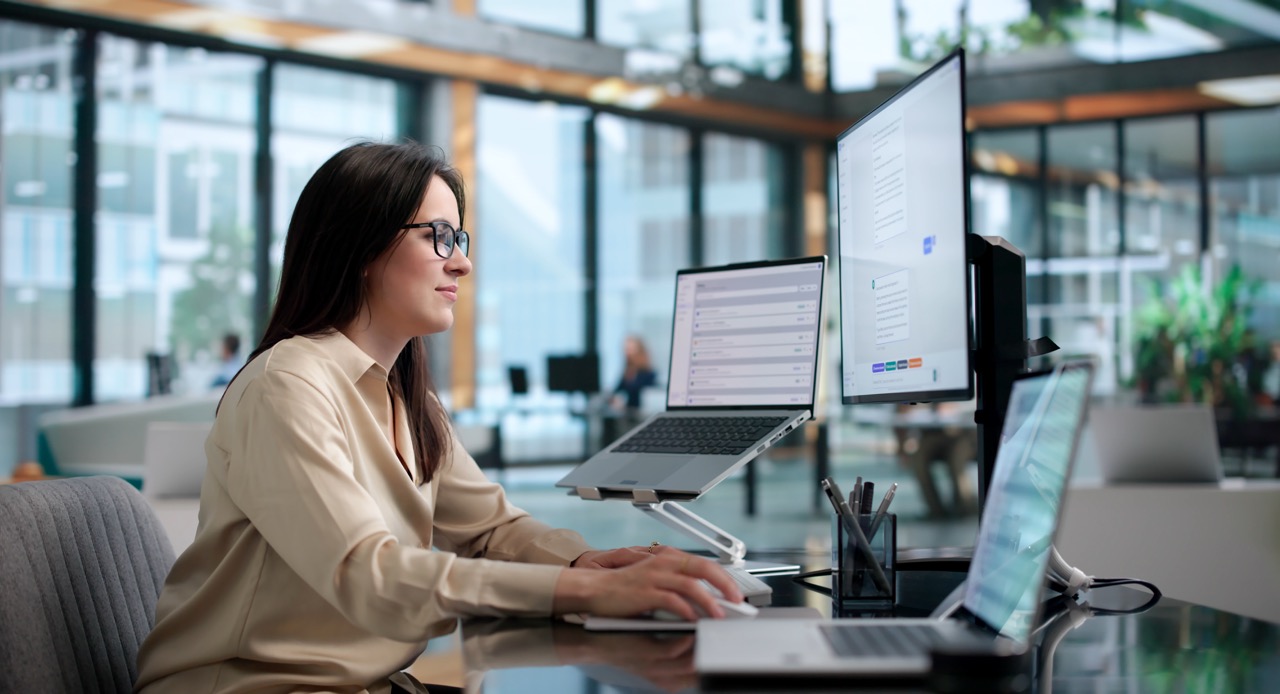 Contact centre agent working across a laptop and two monitors in an open-plan office