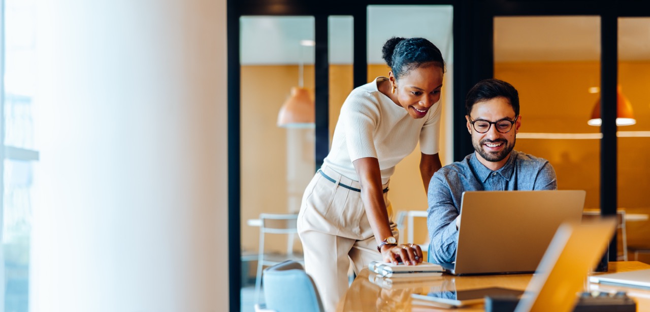 Two colleagues reviewing work together at a laptop in a warmly lit office