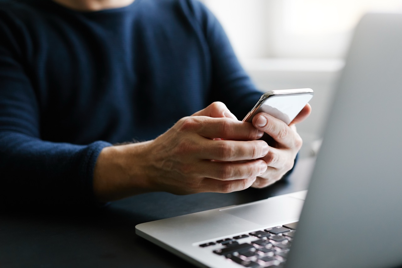 Person holding a mobile phone while working at a laptop