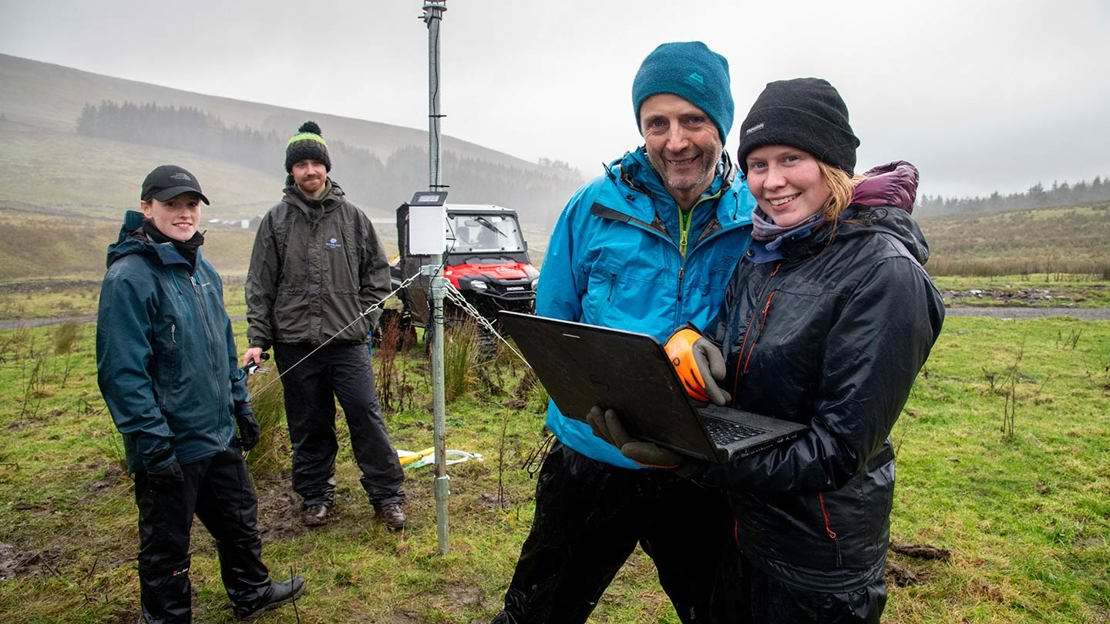 Conservation volunteers gathered around a laptop in open countryside